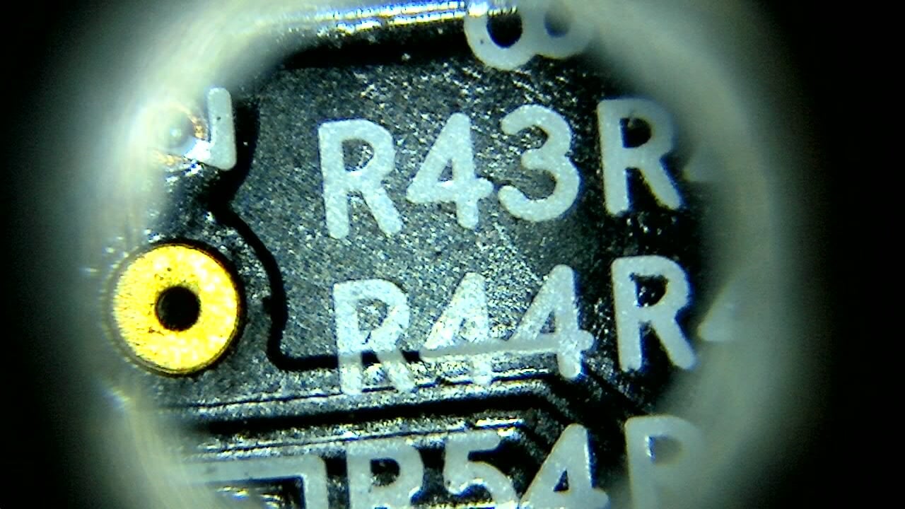 Close-up PCB microscope image showing resistor labels and pad detail